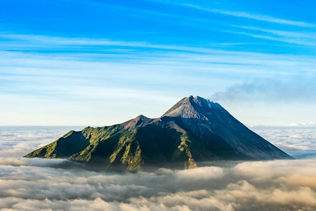 Snow-capped mountain peak rising above a blanket of clouds with a bright blue sky above.