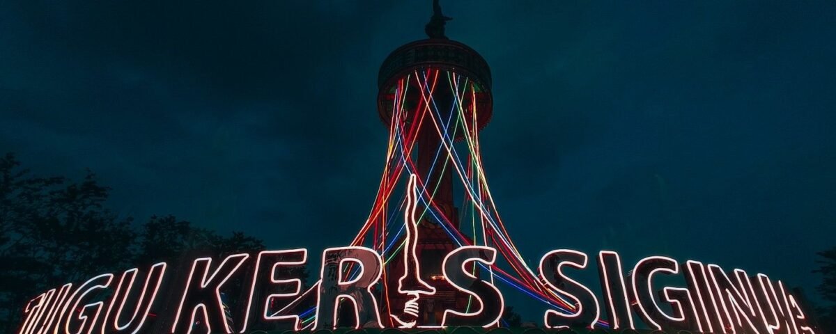 Nighttime scene with a tall tower and a neon sign across a rooftop; multicolor light trails descend from the tower and outline letters across the sign.