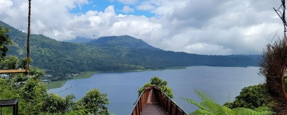 Wooden viewing walkway extends toward a calm lake framed by green hills under a partly cloudy sky.