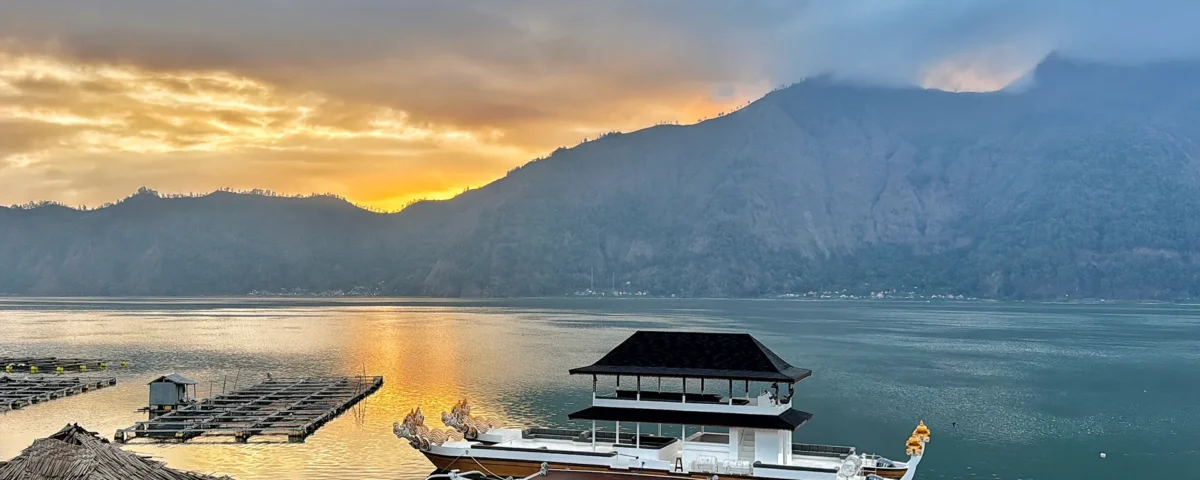 Sunset over a calm lake with a mountain range in the distance and boats docked along wooden piers.