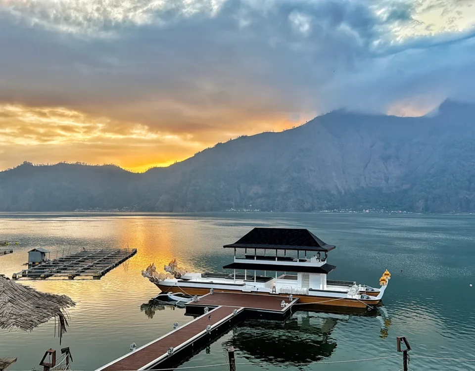 Sunset over a calm lake with a mountain range in the distance and boats docked along wooden piers.
