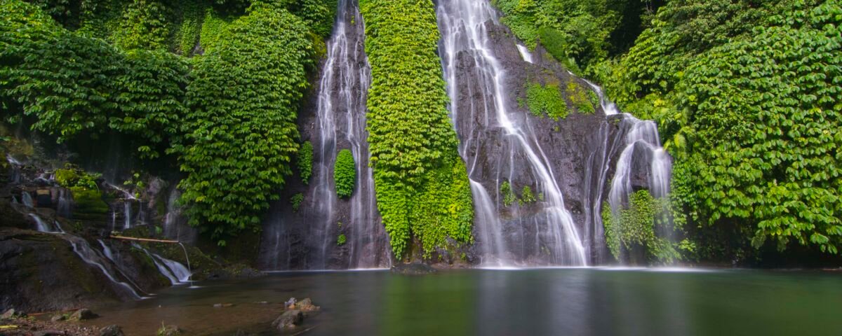 Lush jungle with a multi-tier waterfall cascading down mossy rocks into a calm pool.