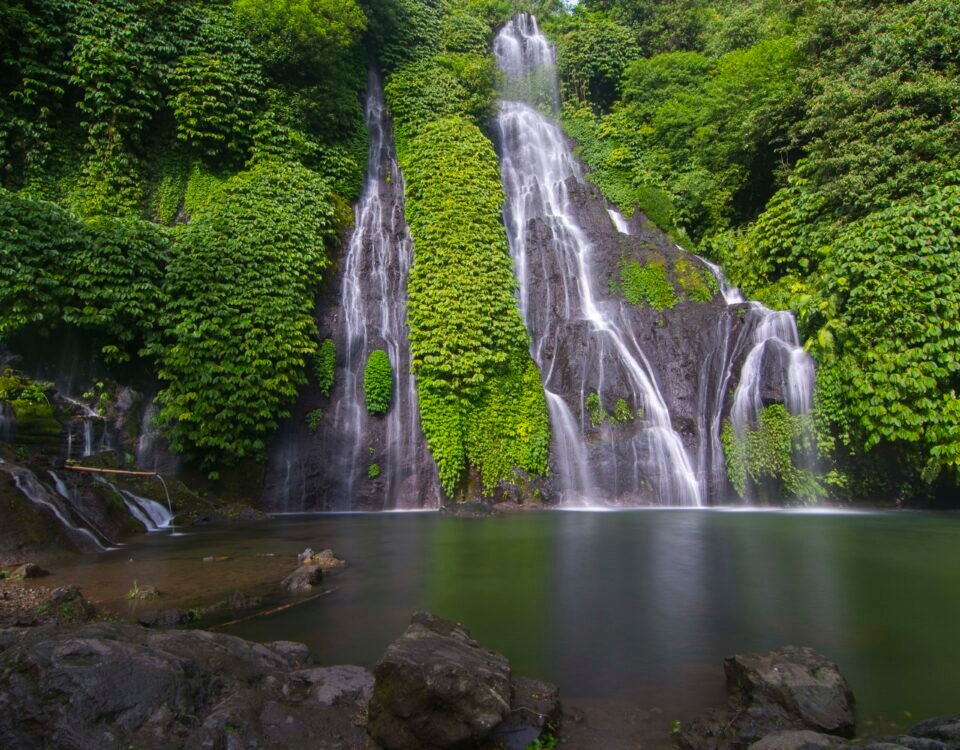 Lush jungle with a multi-tier waterfall cascading down mossy rocks into a calm pool.
