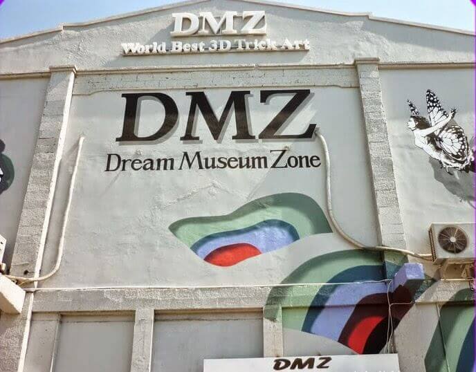 Front of the DMZ Dream Museum Zone building with a large 'DMZ' sign, 'Dream Museum Zone' subtitle, and a colorful abstract mural on the wall.