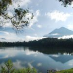 Calm lake reflecting the sky, clouds, and a distant forested mountain.
