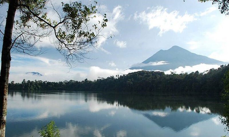 Calm lake reflecting the sky, clouds, and a distant forested mountain.