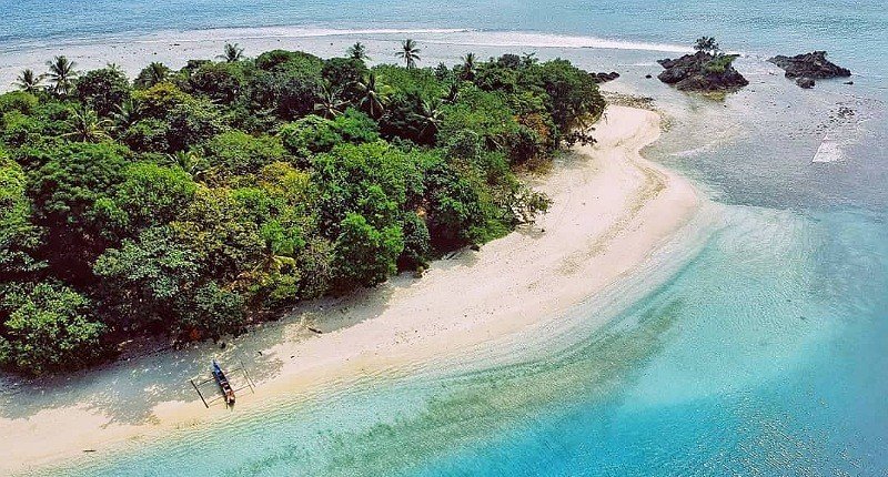 Aerial view of a tropical island with dense green jungle, white sandy beach, and turquoise water along the shore.