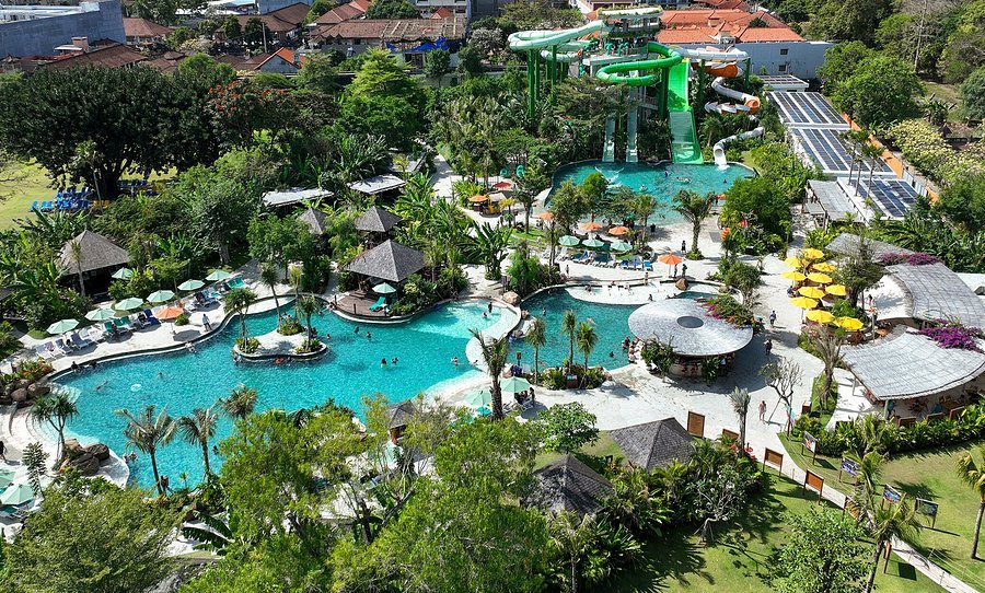 Aerial view of a resort water park with turquoise pools, twisting green slides, and palm trees scattered around.