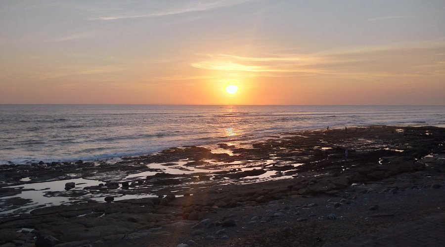 Sunset over the calm ocean with a rocky shoreline and tide pools in the foreground.