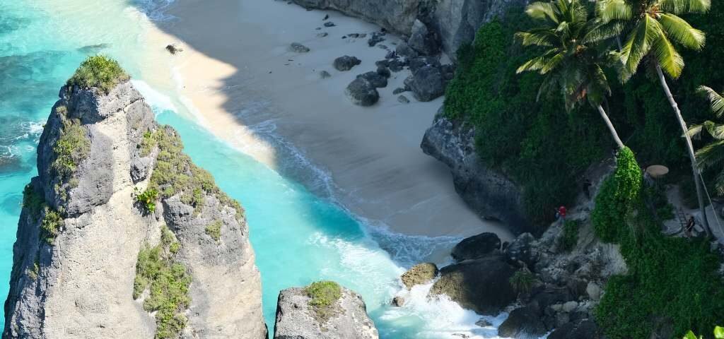 Turquoise water along a sandy cove between tall rocky cliffs and palm trees