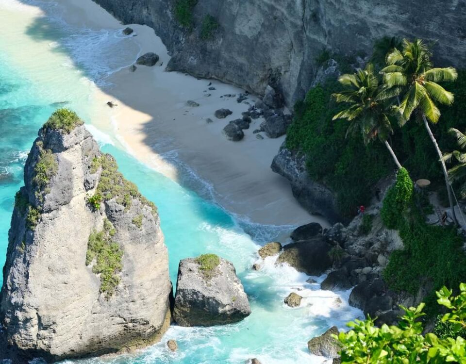 Turquoise water along a sandy cove between tall rocky cliffs and palm trees