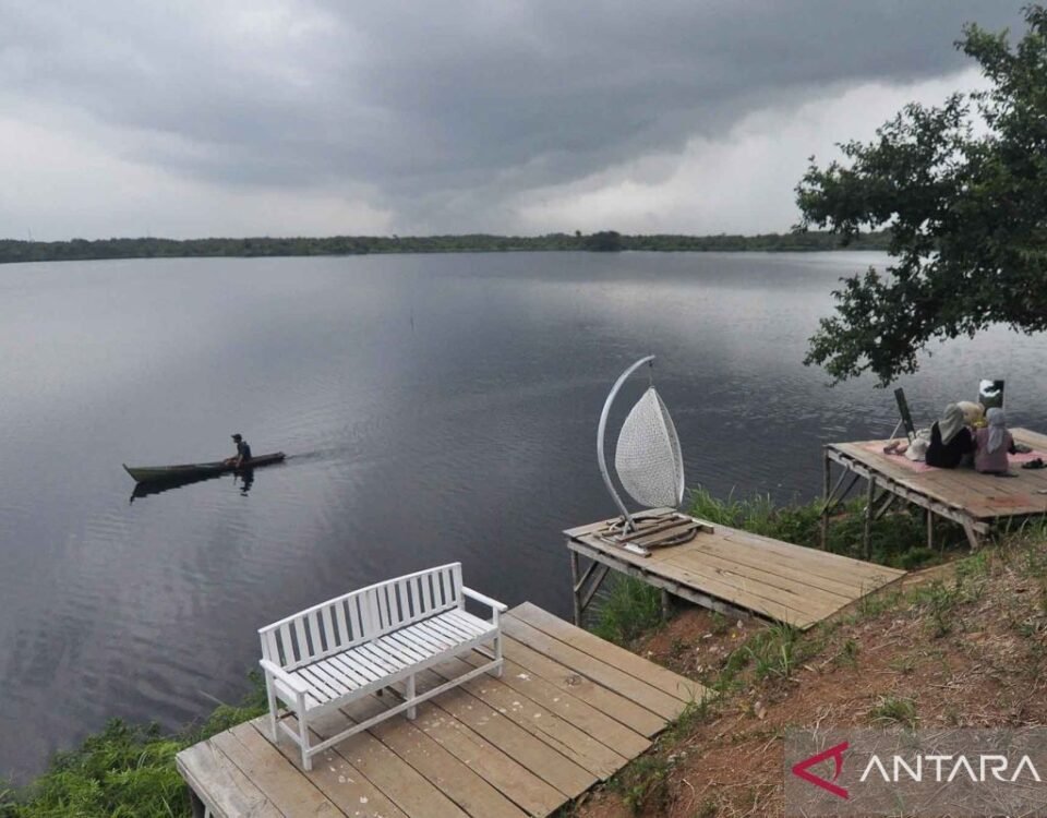 Person paddling a small canoe on a calm, overcast lake with a distant shoreline visible under a cloudy sky.