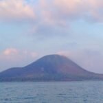 Calm sea with a hill-shaped volcanic island on the horizon and a crowded boat on the right side.