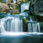 Multi-tiered waterfall cascading over mossy rocks in a rocky gorge setting with emerald mosses on the ledges.