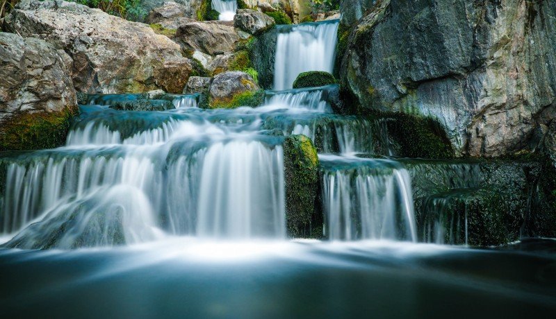 Multi-tiered waterfall cascading over mossy rocks in a rocky gorge setting with emerald mosses on the ledges.