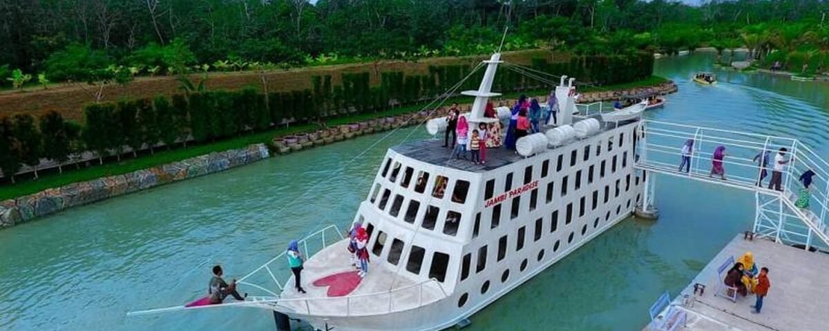 A white multi‑deck passenger ship with many windows sits in a calm green canal, passengers on the upper deck and a gangway connecting to shore nearby.