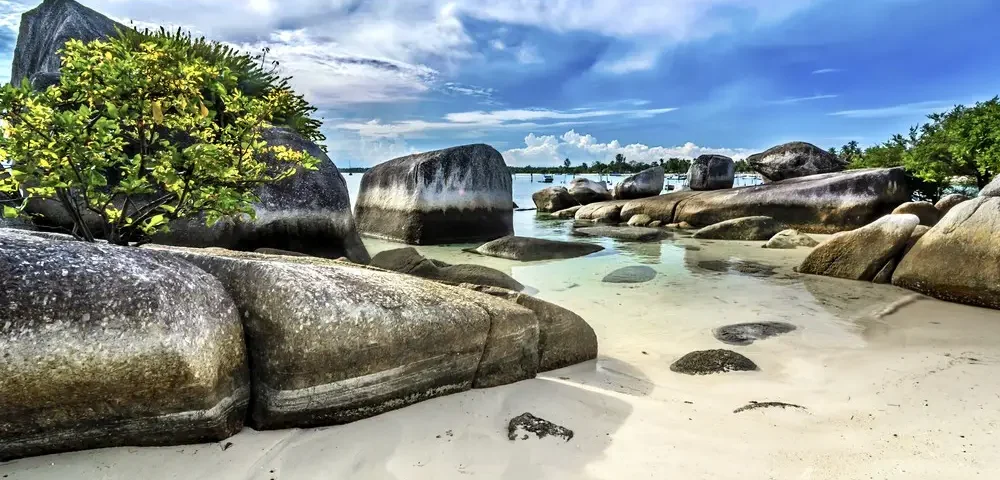 Tropical beach with large granite boulders, white sand, and turquoise water under a blue sky.
