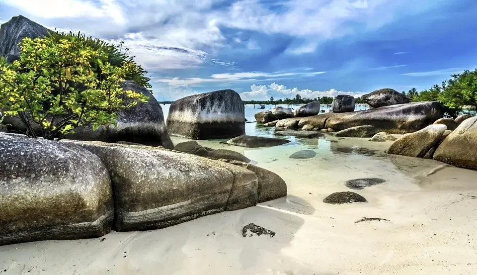 Tropical beach with large granite boulders, white sand, and turquoise water under a blue sky.