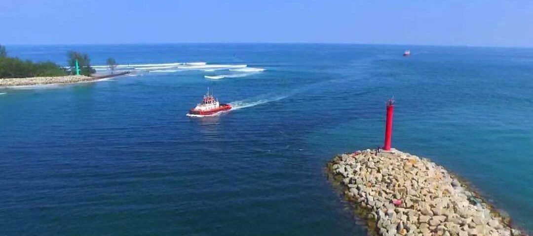 Red lighthouse atop a rocky breakwater extending into calm blue sea, with a small red boat nearby.
