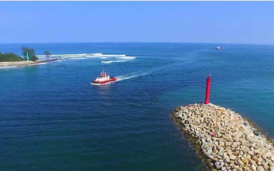 Red lighthouse atop a rocky breakwater extending into calm blue sea, with a small red boat nearby.