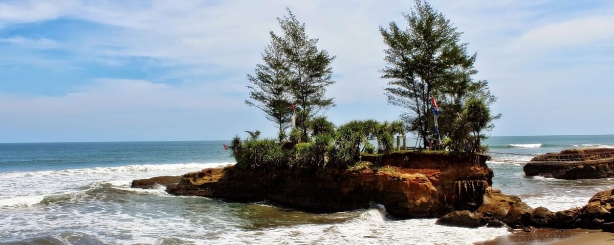 Rocky island covered with palm trees extends into calm blue ocean under a clear sky with gentle waves.