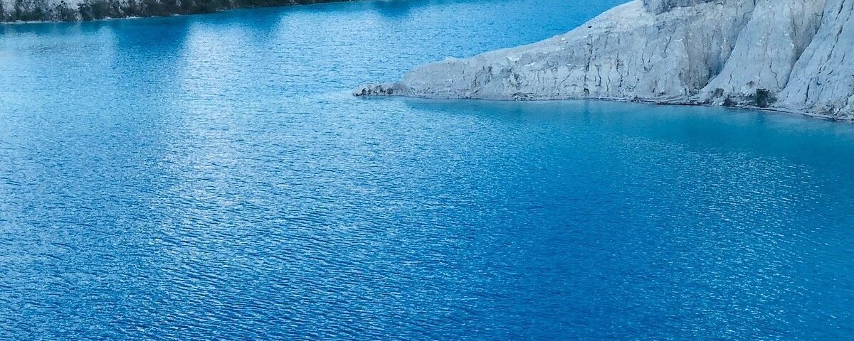 Turquoise lake with white limestone cliffs and an overcast sky in the distance
