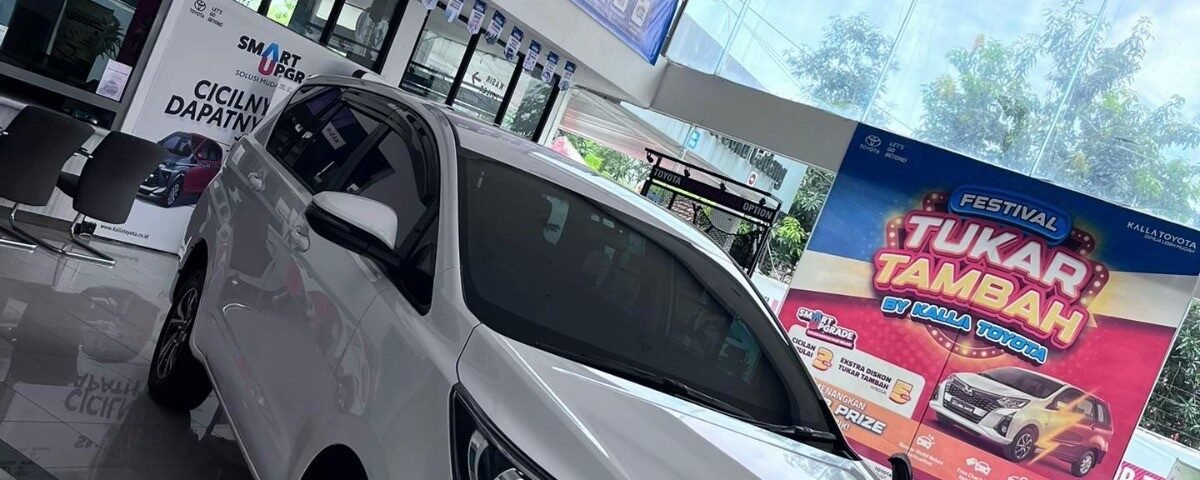 White Toyota SUV on a glossy showroom floor with banners and a large colorful 'Festival Tukar Tambah' poster in the background.