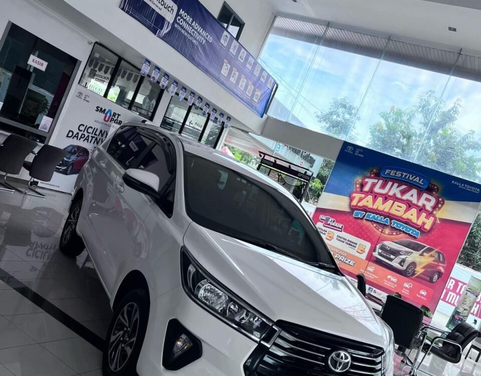 White Toyota SUV on a glossy showroom floor with banners and a large colorful 'Festival Tukar Tambah' poster in the background.