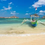 Colorful wooden outrigger boat anchored on a sandy tropical beach with turquoise water and a bright blue sky.