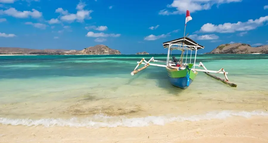 Colorful wooden outrigger boat anchored on a sandy tropical beach with turquoise water and a bright blue sky.