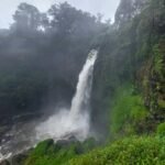 Waterfall plunging down a mossy cliff into a misty pool, surrounded by lush green vegetation.