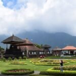 Temple complex by a calm lake with traditional pagoda-style roofs and neatly trimmed gardens, mountains in the distance