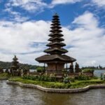 Multi-tiered stone pagoda on a small island in a lake, with sky and distant hills in the background.