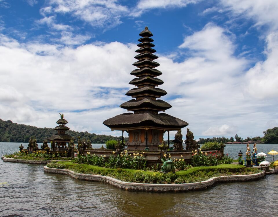 Multi-tiered stone pagoda on a small island in a lake, with sky and distant hills in the background.