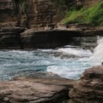 Layered rock cliffs along a rugged coastline as blue waves crash onto rocks at shore.5)