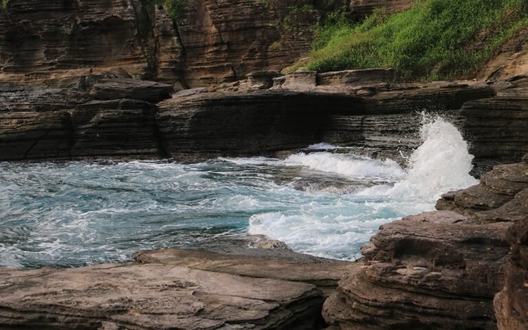 Layered rock cliffs along a rugged coastline as blue waves crash onto rocks at shore.5)