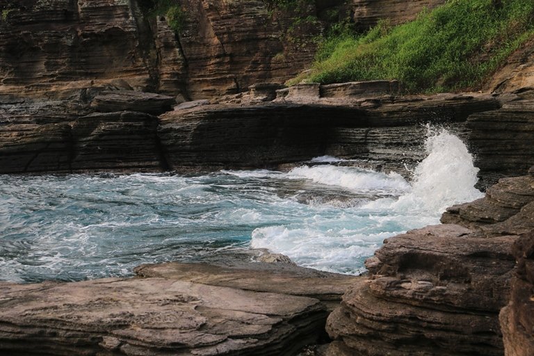 Layered rock cliffs along a rugged coastline as blue waves crash onto rocks at shore.5)