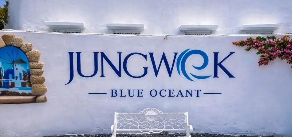 White wall sign reading 'JUNGWOOK BLUE OCEAN' with a blue dome and a decorative white bench in front on a stone-paved courtyard.