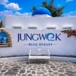 White wall sign reading 'JUNGWOOK BLUE OCEAN' with a blue dome and a decorative white bench in front on a stone-paved courtyard.