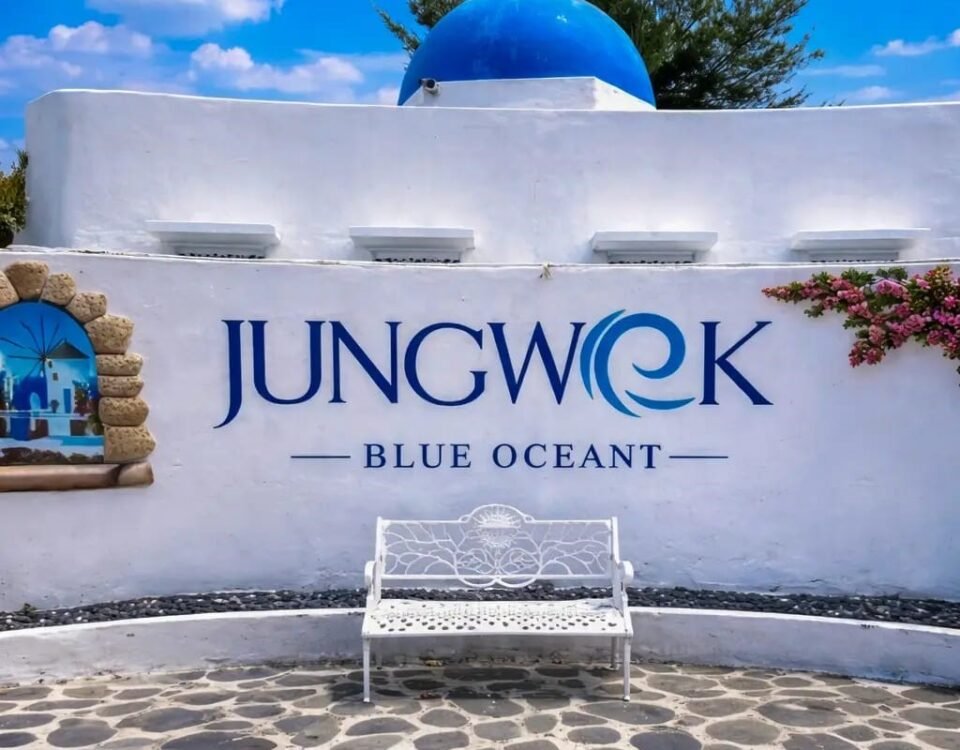 White wall sign reading 'JUNGWOOK BLUE OCEAN' with a blue dome and a decorative white bench in front on a stone-paved courtyard.