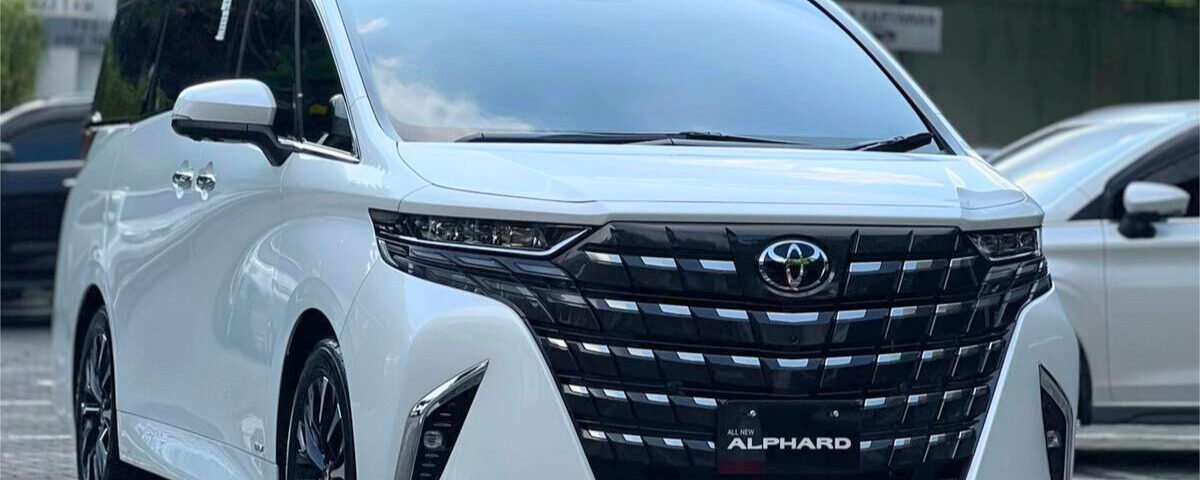 Front three-quarter view of a white Toyota Alphard minivan parked, showing the large black grille, chrome trim, and 'All New Alphard' badge.
