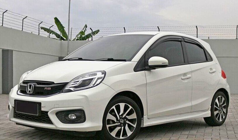 White Honda hatchback parked on a paved surface, shown from a front-three-quarter angle with alloy wheels and tinted windows.