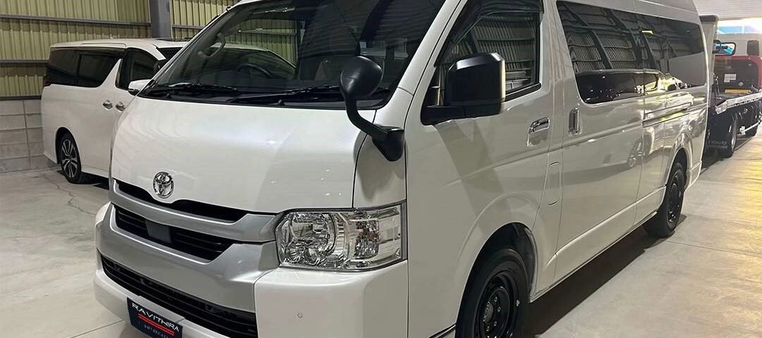 White Toyota van in a showroom, front three-quarter view, clean and polished interior lighting reflecting off the body