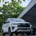 White Toyota SUV parked in an outdoor lot beside a metal warehouse, with DYAN TRANSPORT logos visible on the image.