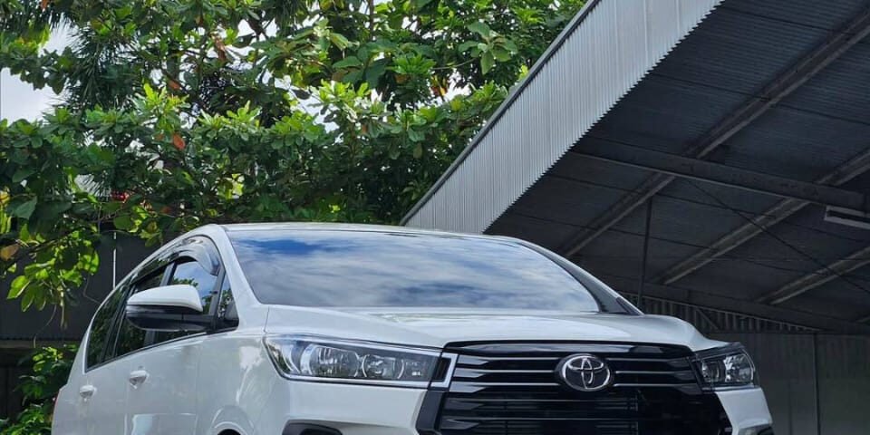 White Toyota SUV parked in an outdoor lot beside a metal warehouse, with DYAN TRANSPORT logos visible on the image.