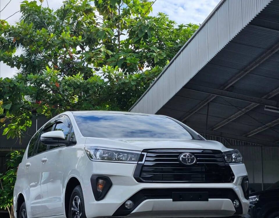 White Toyota SUV parked in an outdoor lot beside a metal warehouse, with DYAN TRANSPORT logos visible on the image.