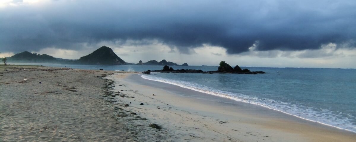 Desolate beach with wet sand and calm water under a looming dark storm cloud over distant rocky headlands