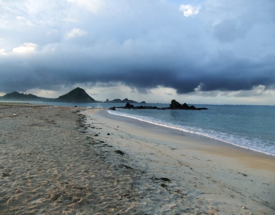 Desolate beach with wet sand and calm water under a looming dark storm cloud over distant rocky headlands
