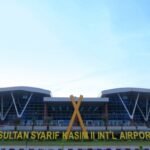 Sultan Syarif Kasim II International Airport terminal with a large yellow sign reading the airport name in front of glass façade.