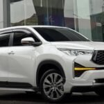 White Toyota SUV parked outside a modern glass-front dealership with the Toyota logo above it.
